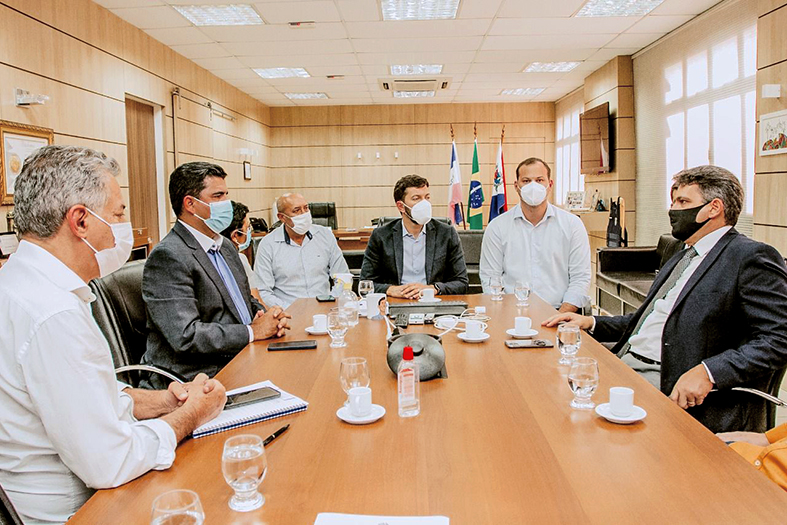Seis homens de máscara conversam em uma sala de reuniões.