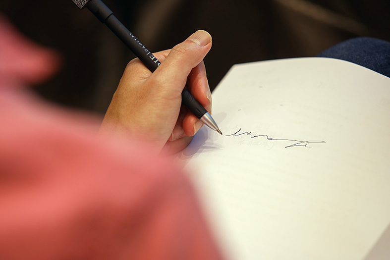 Detalhe de mão de mulher assinando com uma caneta de cor preta em um caderno em branco