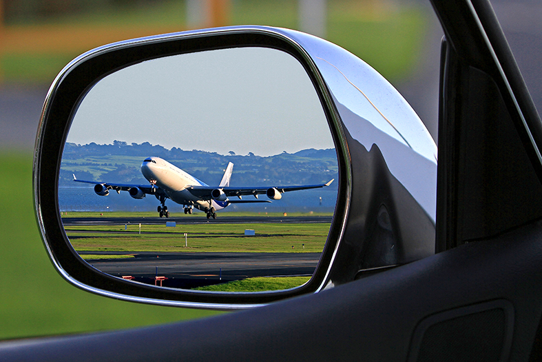 Reflexo em um retrovisor de carro mostra avião decolando.