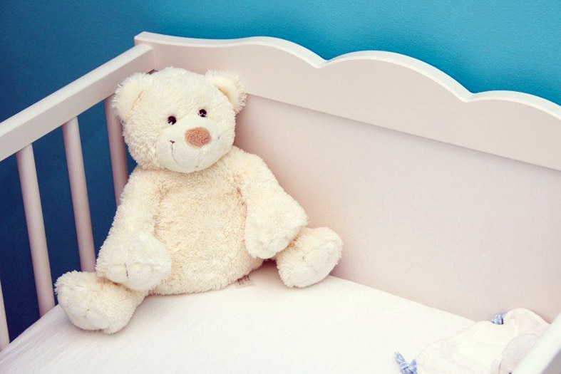 Detalhe de um berço na cor branca. Repousado na cama, um urso de pelúcia branco.