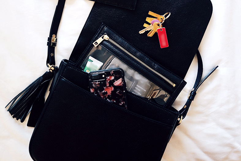 Bolsa feminina de cor preta aberta com celular, carteira e chaves a mostra.