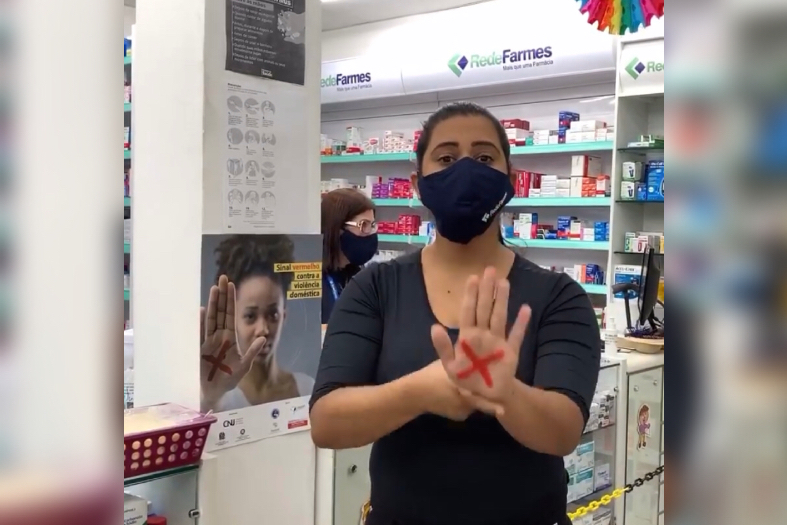 mulher em farmácia mostrando a palma da mão com um X em vermelho