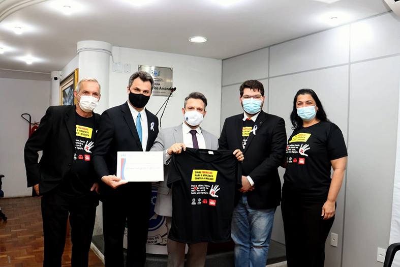 cinco pessoas, quatro homens e uma mulher posam para foto segurando camisetas da campanha sinal vermelho.