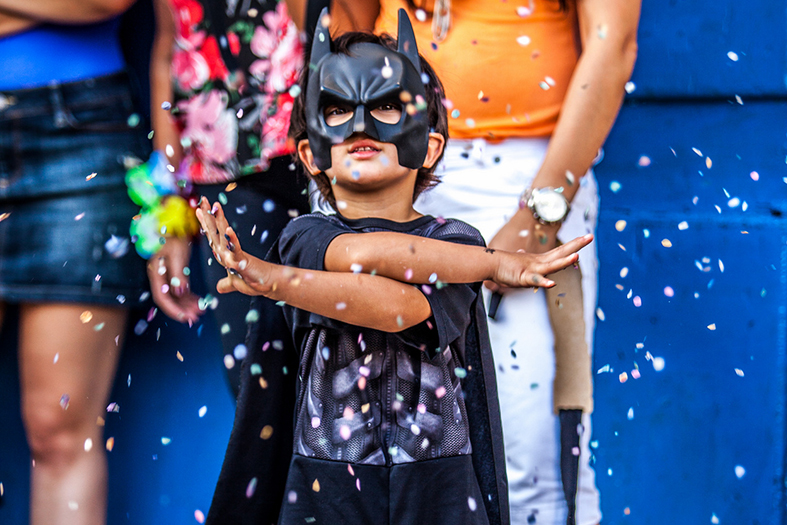 Criança fantasiada pula carnaval em meio a adultos.