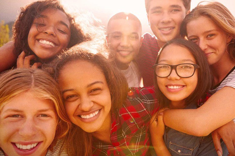 Grupo de adolescentes sorriem e se abraçam olhando para frente.
