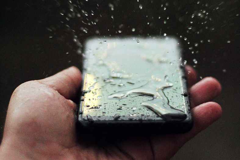 Detalhe de mão masculina segurando um celular totalmente molhado.