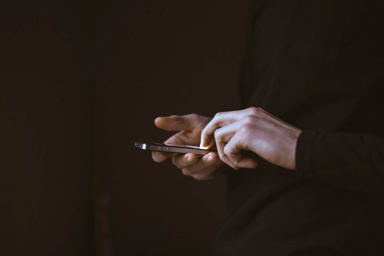 Ambiente escuro ou com pouca luz. em destaque mãos masculinas operando um celular smartphone.