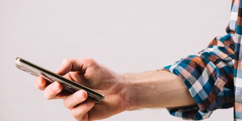 Mão de um homem segura um celular do tipo smartphone.