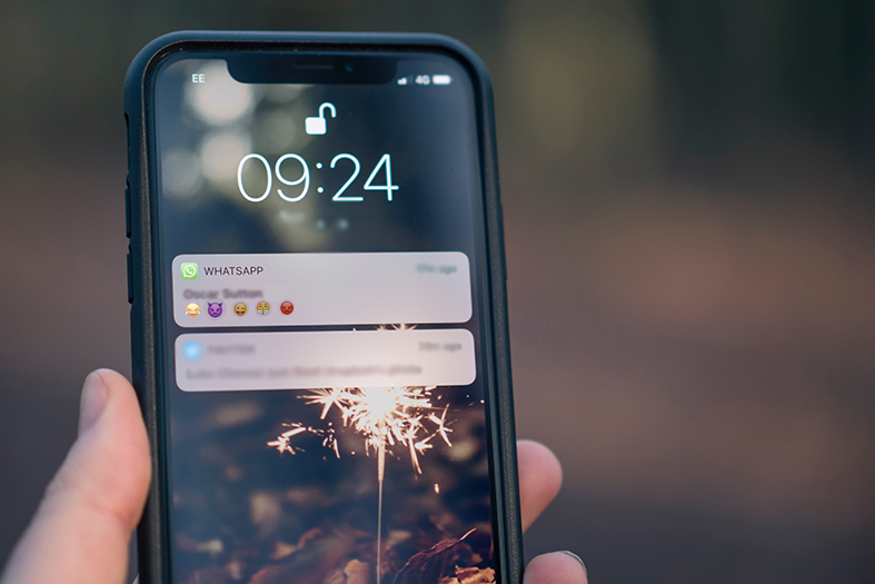Detalhe de mão de homem segurando um celular cuja tela mostra uma notificação de whastapp.