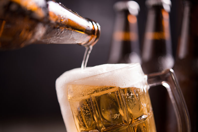 Detalhe da boca de uma garrafa de cerveja enchendo um copo até a borda.