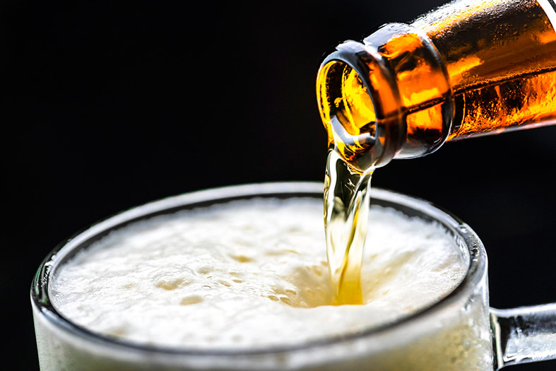 Detalhe da boca de uma garrafa de cerveja enchendo um copo até a borda.