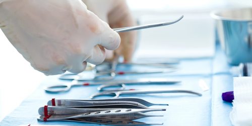 Detalhe de instrumentos de cirurgia sendo manipulados por mãos com luvas.