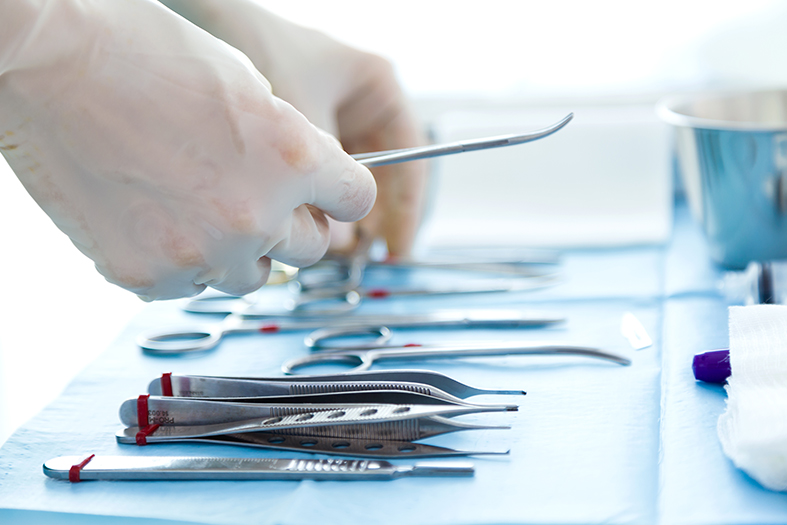 Detalhe de instrumentos de cirurgia sendo manipulados por mãos com luvas.