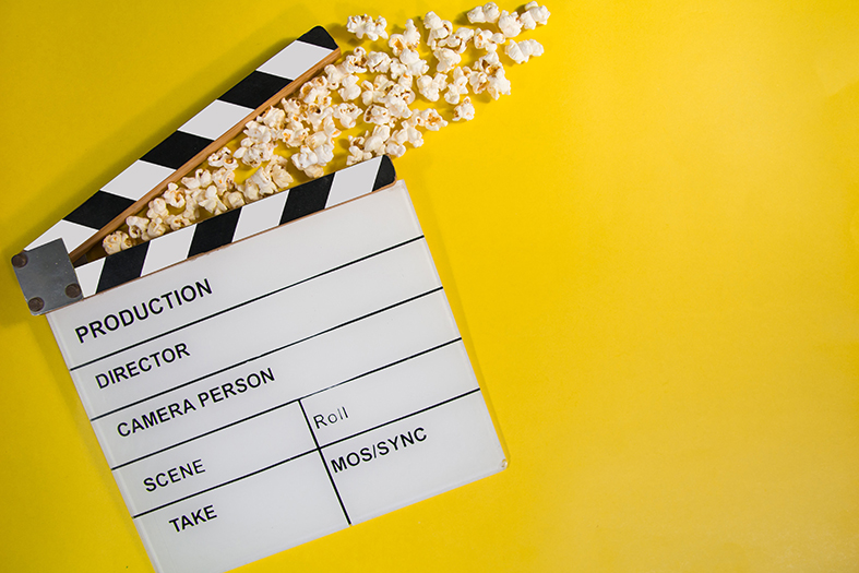Claquete de cinema de cor branca sobre fundo amarelo.