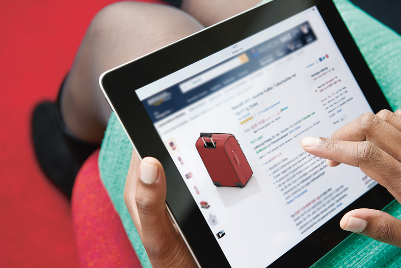 Mulher realiza compra de bagagens online através de tablet repousado em seu colo.