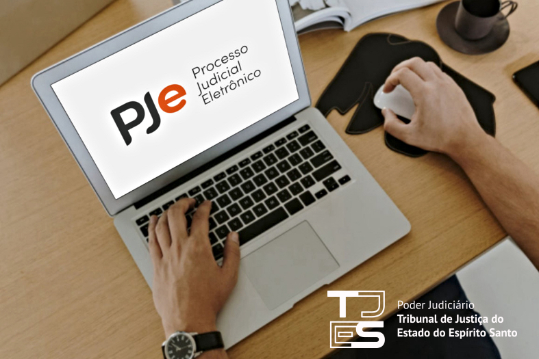 Fotografia dos braços de uma pessoa utilizando um laptop. Na tela, sobre um fundo branco, está projetado o logotipo do Pje e ao lado dele o texto "Processo Judicial Eletrônico".