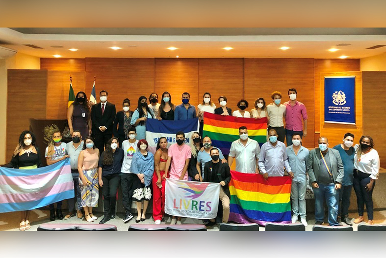 Um grupo grande de pessoas segurando bandeiras da representatividade lgbtqia+ posa para foto.