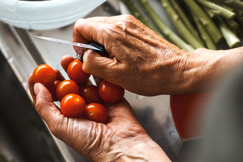 detalhes de mãos de pessoa idosa limpando tomates cereja em uma pia.