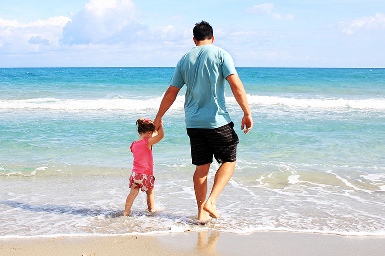 pais e filha pequena caminham em uma praia sem ninguém por perto
