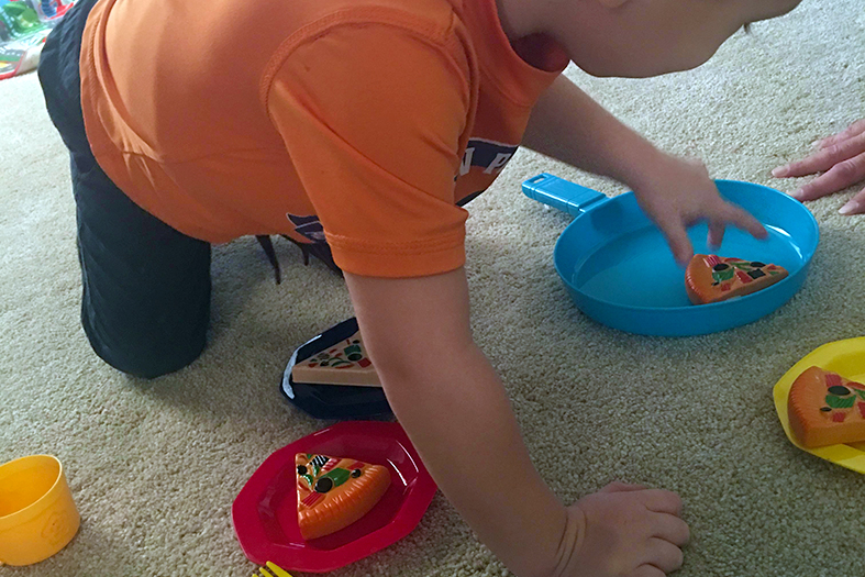 Criança do sexo masculino brincando com objetos coloridos no chão de uma sala.
