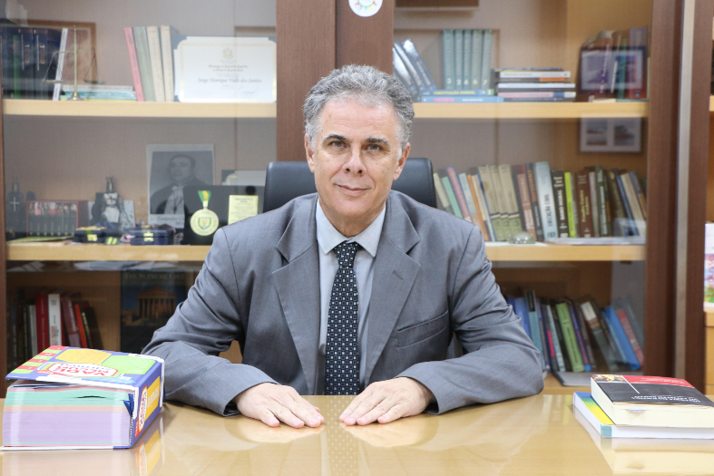 O desembargador Jorge Henrique Valle, homem e pele branca e cabelos grisalhos. Ele está em seu gabinete e veste terno na cor cinza.