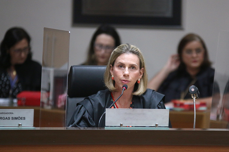 A desembargadora Marianne Júdice de Mattos é uma mulher de pele branca, com cabelos loiros. Ela veste uma beca na cor preta.