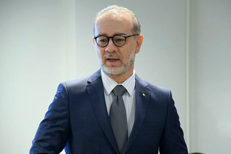 homem branco, calvo, de barba e cabelos grisalhos. ele está usando terno na cor azul marinho e gravata cinza chumbo.