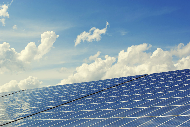 Painéis solares refletindo o céu azul com nuvens brancas.