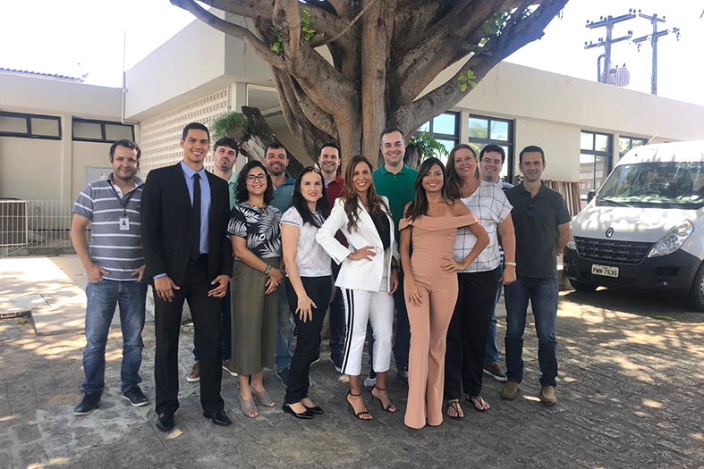 Grupo de pessoas possa para fotografia em frente a uma frondosa árvore.