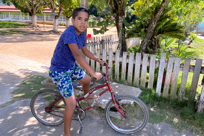 menino de pele parda, estatura mediana, cabelos pretos e camisa azul escura com bermuda estampada.