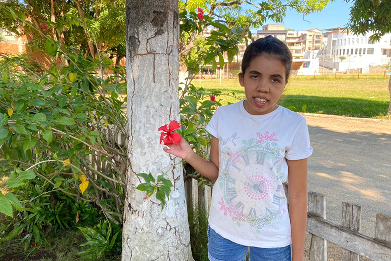 menina parda de estatura baixa e cabelos pretos. ela usa uma bermuda jeans e uma camiseta com estampas claras.