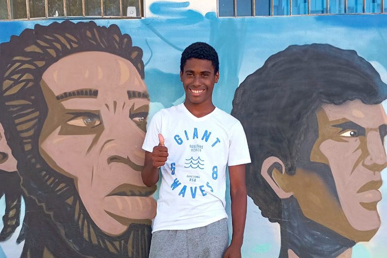 Adolescente de cor negra sorri e faz sinal de positivo com a mão.