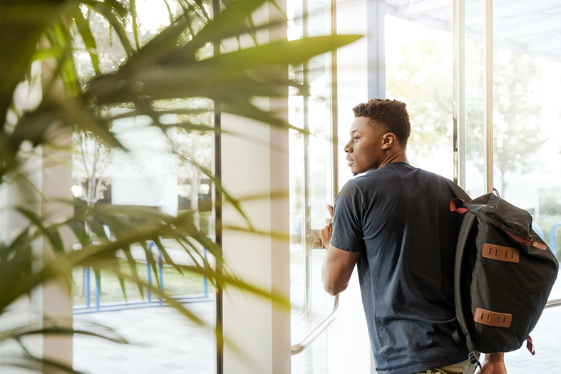 Homem jovem de pele negra carregando mochila em suas costas.