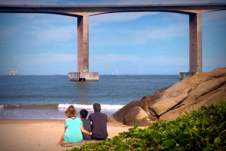 Pessoas de costas admirando a enseada do suá e a vista da terceira ponte.