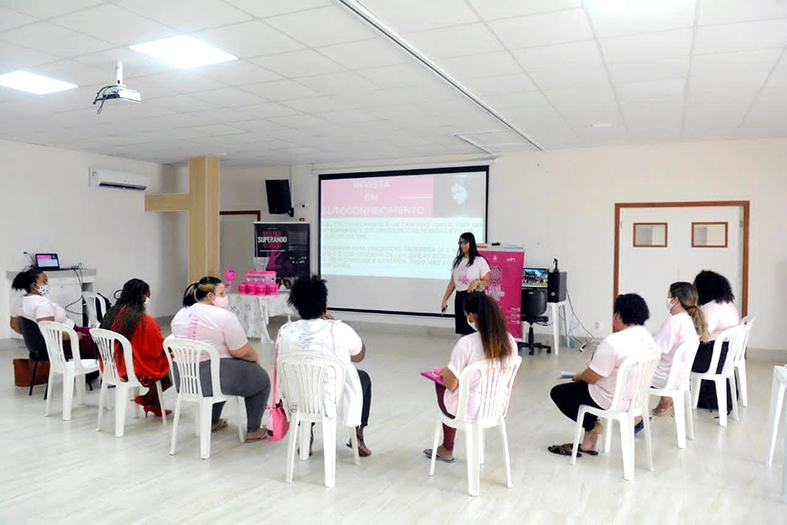 grupo de mulheres sentadas em cadeira fazendo um semicírculo assistindo a uma mulher dando uma aula.