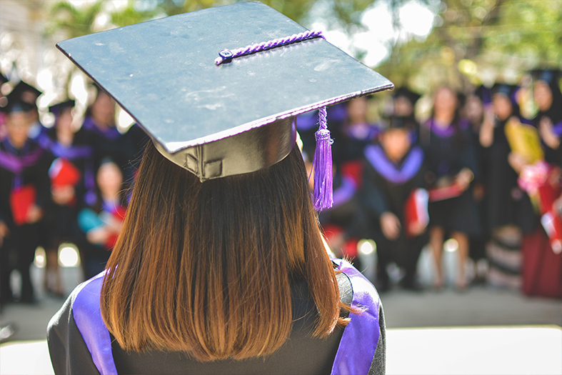 Jovem mulher de costas com as vestimentas típicas de uma formatura universitária.