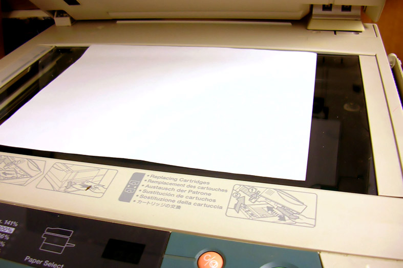 Detalhe de uma fotocopiadora com o tampo aberto e uma folha em branco