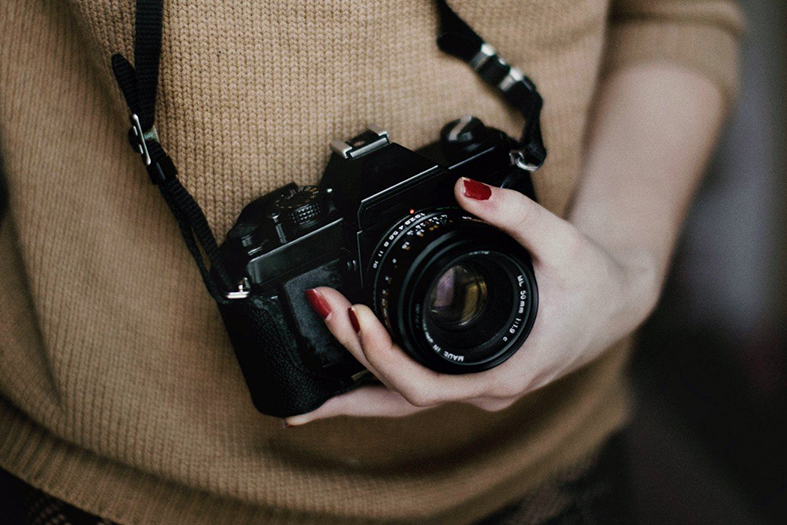 Detalhe de mulher segurando uma câmera fotográfica profissional.