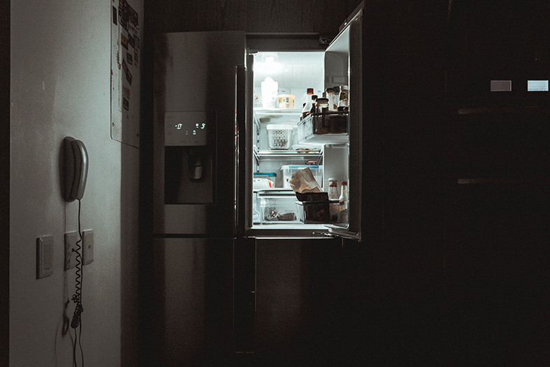 Cozinha escura a não ser pela iluminação que vem de dentro da geladeira aberta.