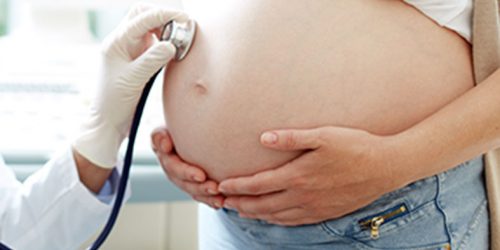 Um médico colocando um estetoscópio na barriga de uma grávida.