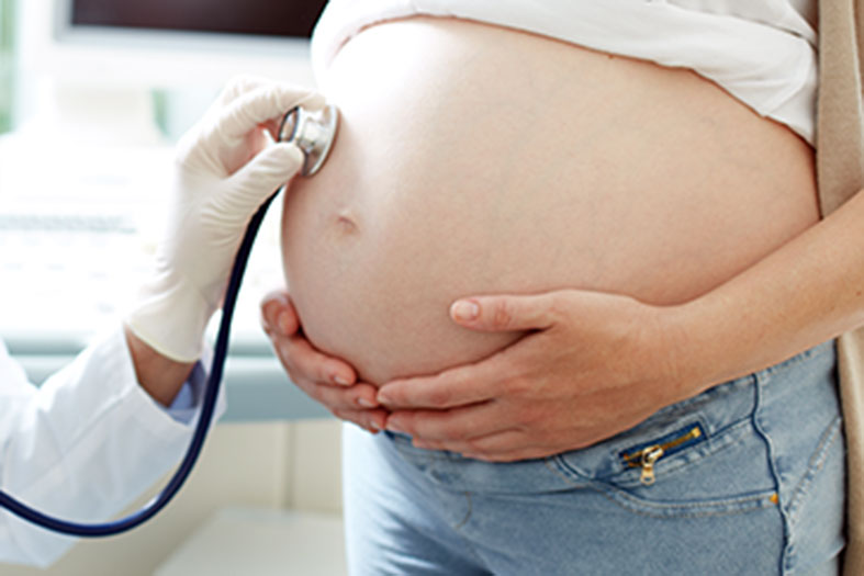 Um médico colocando um estetoscópio na barriga de uma grávida.