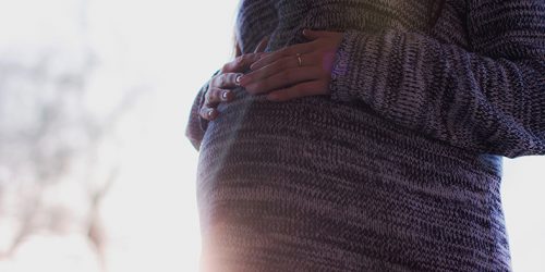 Detalhe de uma mulher segurando sua barriga indicando gravidez.