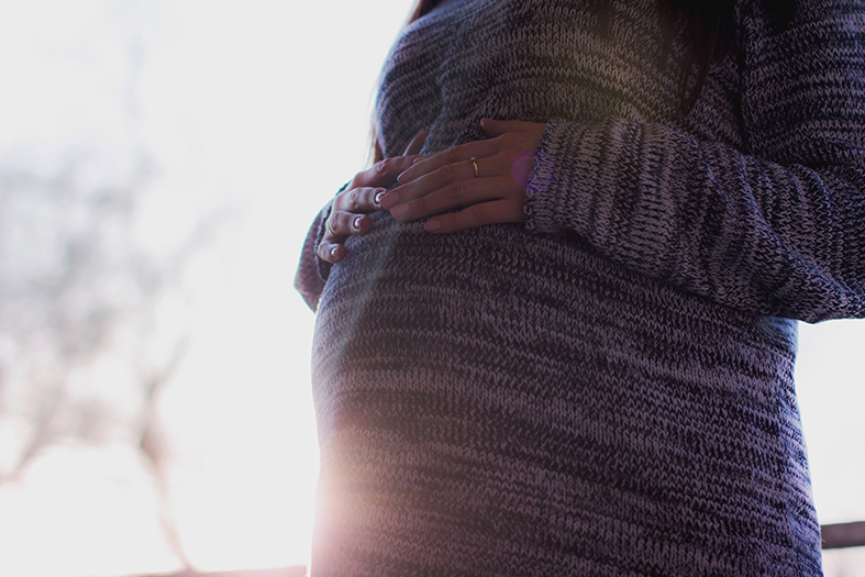 Detalhe de uma mulher segurando sua barriga indicando gravidez.