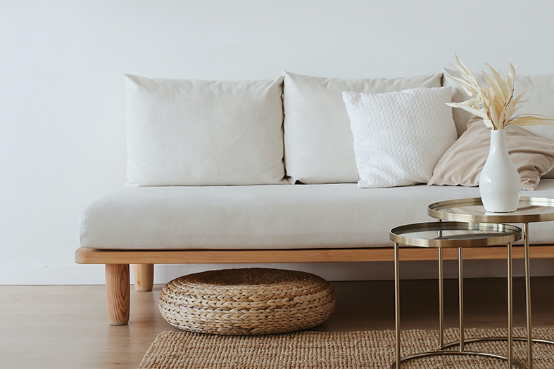 detalhe de sofá, mesa de centro e descanso para os pés de um apartamento cuja parede está pintada de branco.