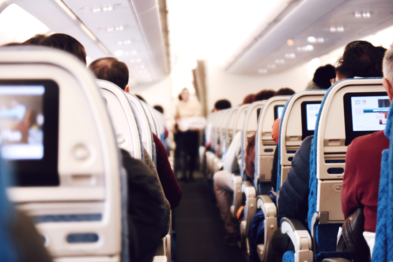 Visão de trás para frente de um corredor de uma aeronave onde se vê somente as costas dos assentos e o topo das cabeças dos passageiros.