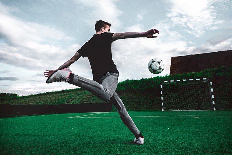 Adolescente do sexo masculino chuta uma bola de futebol em direção ao gol.