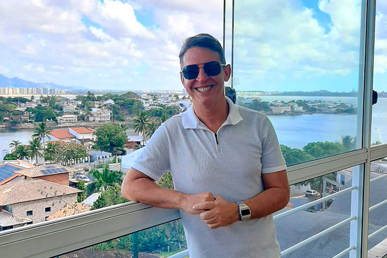 Foto do psicólogo escolar e neuropsicólogo Marcelo Batista, homem de pele branca e cabelos na cor preta. Ele usa camisa polo, óculos escuros e sorri para a câmera.