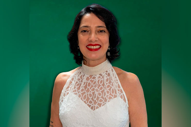 A professora Jeane Martins, mulher branca com cabelos na cor preta. Ela veste um vestido branco de renda.