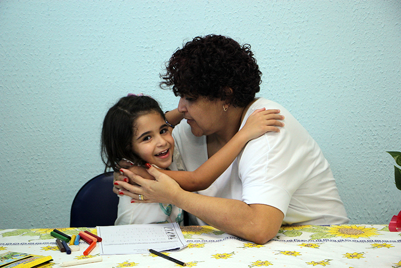 Mãe e filha sentadas à mesa e se abraçando.