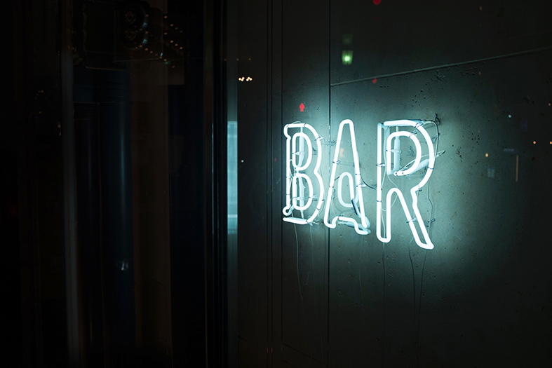 Em parede pouco iluminada um letreiro em neon azul com a palavra bar.
